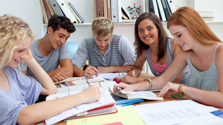 Fünf Jugendliche sitzen gemeinsam am Tisch, lesen oder arbeiten in Ordnern.