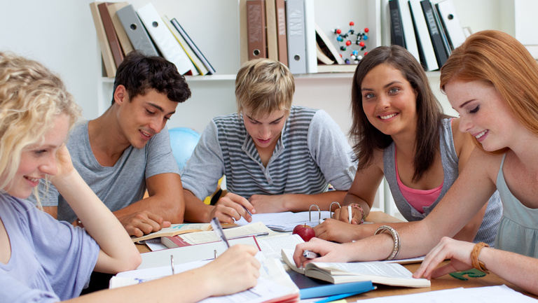 Fünf Jugendliche sitzen gemeinsam am Tisch, lesen oder arbeiten in Ordnern.