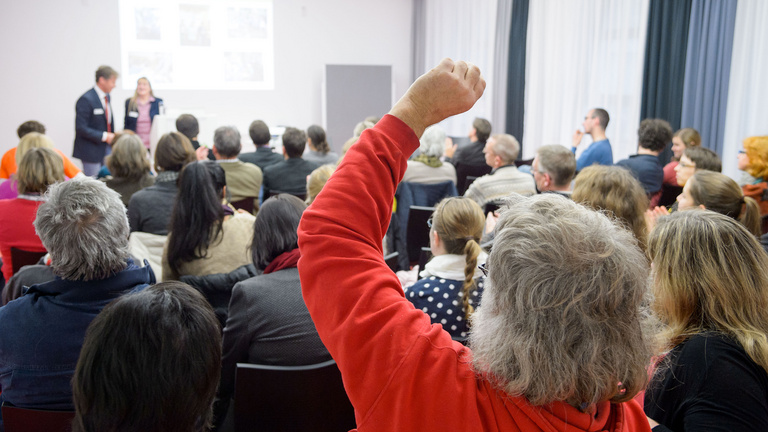 Lehrende bilden Lehrende Lehrerinnen und Lehrer sitzen in einem Vortragsraum. Sie hören zwei Vortragenden zu oder melden sich für eine Wortbeitrag.