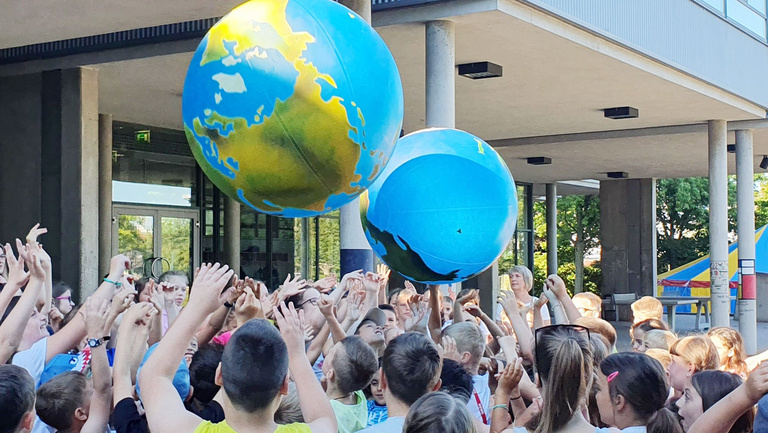 „WELTfairÄNDERER“ schulen Verantwortungsbewusstsein Viele Kinder stehen eng zusammen und werfen Erdbälle in die Luft.