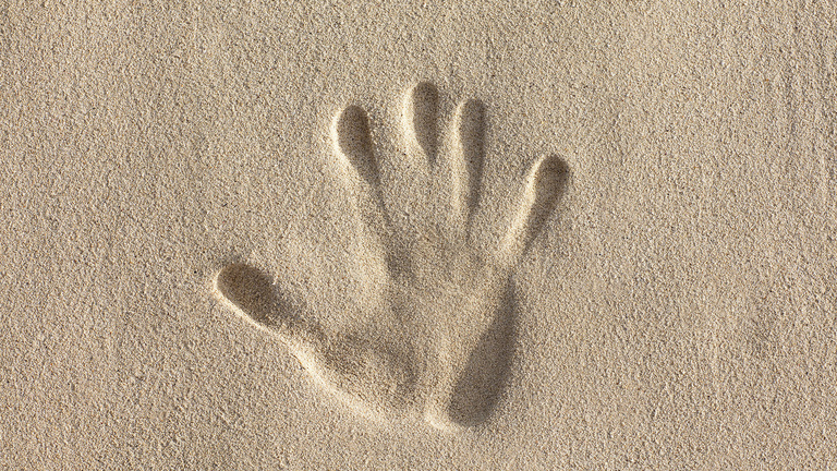 Ein Abdruck einer rechten Hand im Sand.