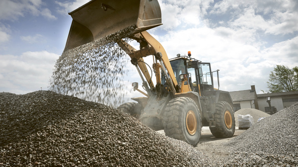 Dargestellt ist ein Bagger, der mit seiner Schaufel eine Ladung Schotter ablässt.
