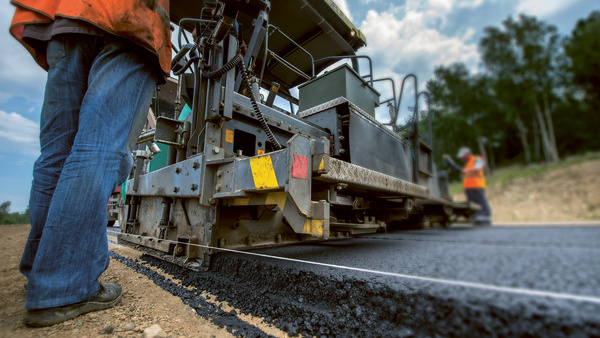 Dargestellt ist eine Szene im Straßenbau, eine Straße wird asphaltiert.