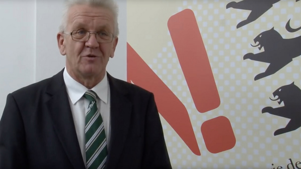 Die Nachhaltigkeitsberater Ministerpräsident Kretschmann steht vor einer Rückwand mit dem Logo der Nachhaltigkeitsstrategie Baden-Württemberg.