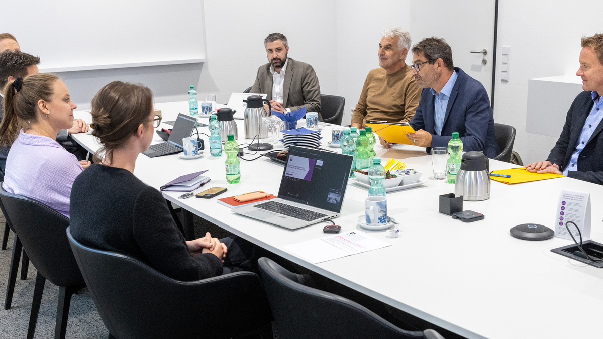Staatssekretär Dr. Baumann sitzt mit mehreren Personen an einem Tisch in einem intensiven Gespräch.