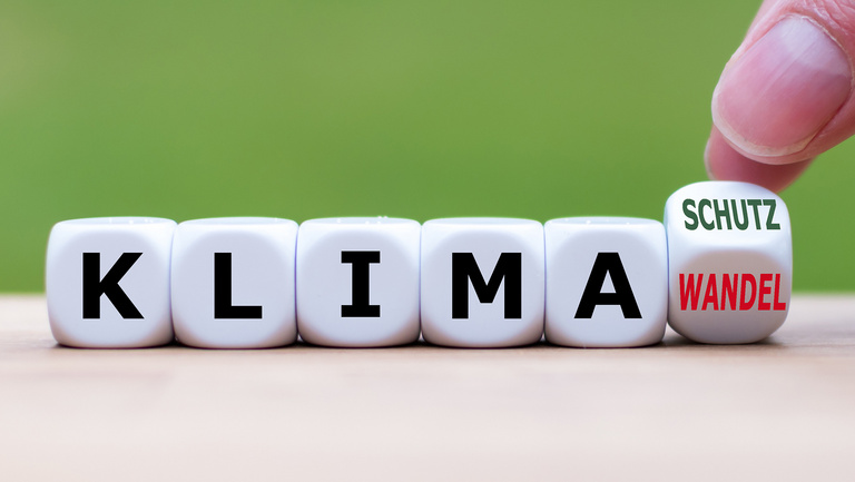 Klimawandel - Klimaschutz Fünf Spielwürfel mit Buchstaben bilden das Wort Klima. Auf einem letzen Würfel in der Reihe steht auf einer Würfelfläche das Wort Wandel und auf der anschließenden das Wort Schutz. Dieser Würfel wird von zwei Fingern auf Kippstellung zwischen Wandel und Schutz gehalten.