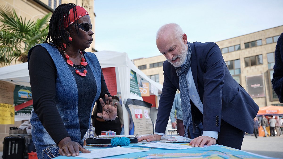 Eine Frau und ein Mann stehen um einen Tisch, auf dem eine große Weltkarte liegt.