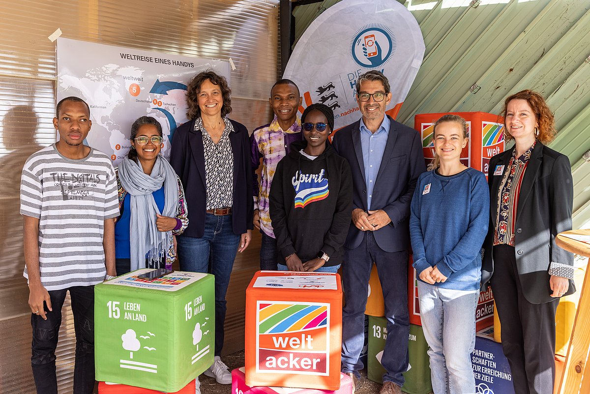 Mehrere Personen stehen nebeneinander innerhalb des Standes der Handy-Aktion BW. Hinter Ihnen ist eine dazu passende Flagge aufgestellt und rings herum große bunte Würfel mit Aufschrift.