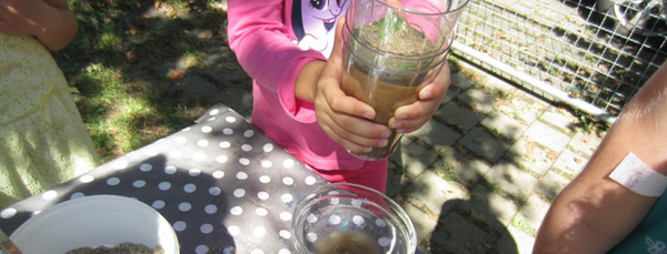 Drei Kindergartenkinder stehen um einen Tisch und reinigen Wasser mit einem selbstgebauten Filter.