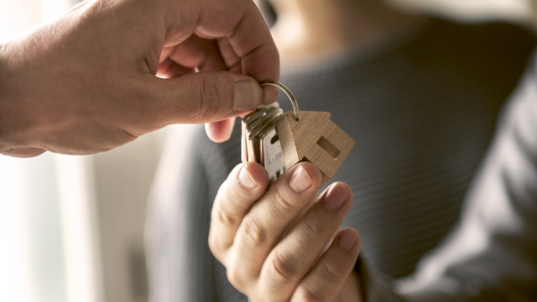 Dargestellt ist eine Szene, bei der eine Person einer anderen einen Schlüssel übergibt.