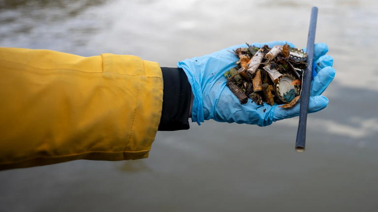 Eine Hand, die Müll aus einem Fluss sammelt.