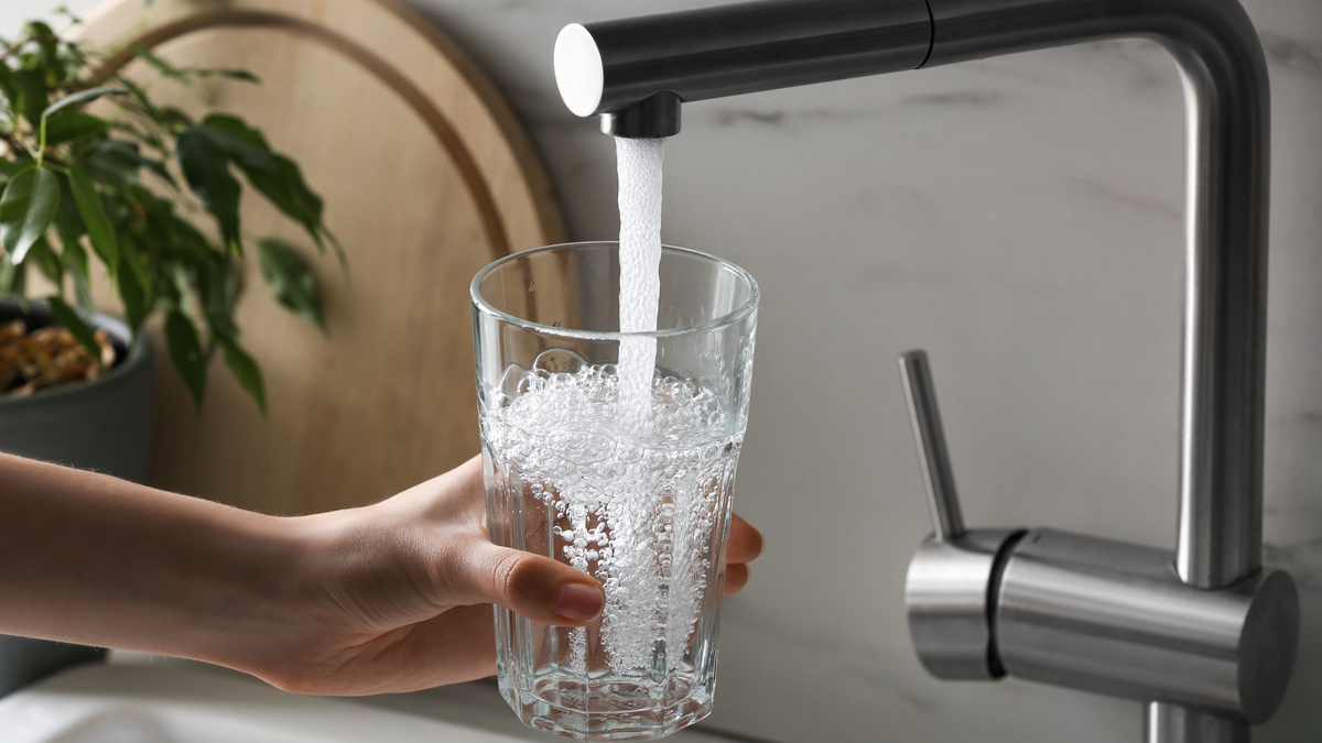 Wasser Marsch Eine Person hält ein Glas unter den laufenden Wasserhahn.