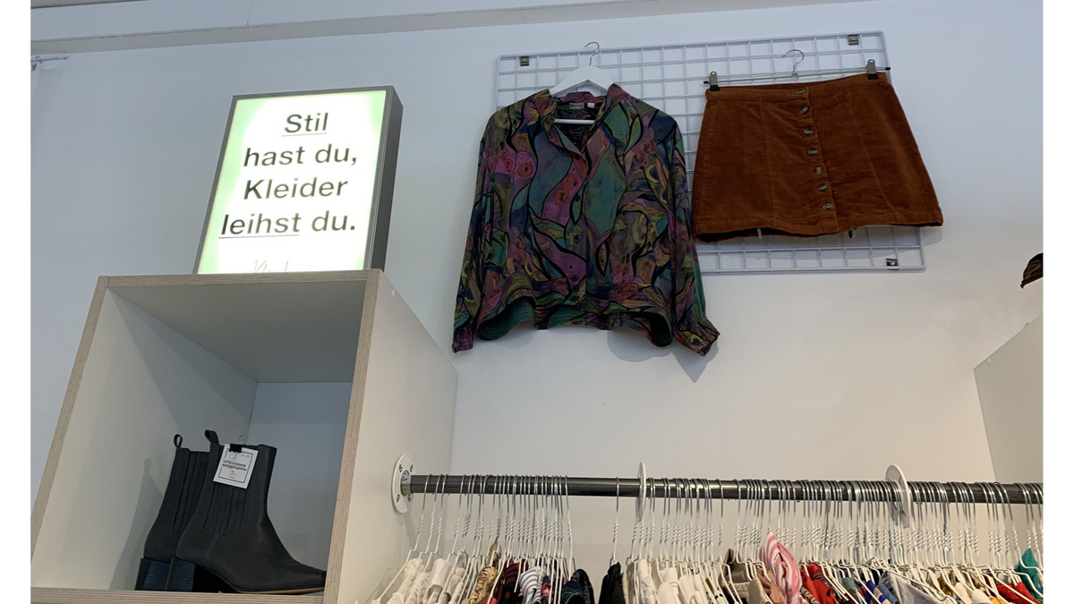 Stil hast du, Kleider leihst du. In der Kleiderei steht auf einem Regal eine Leuchtreklame mit dem Text: Stil hast du, Kleider leihst du.